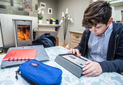 Een jongen studeert aan de salontafel. Hiervoor gebruikt hij zijn tablet.