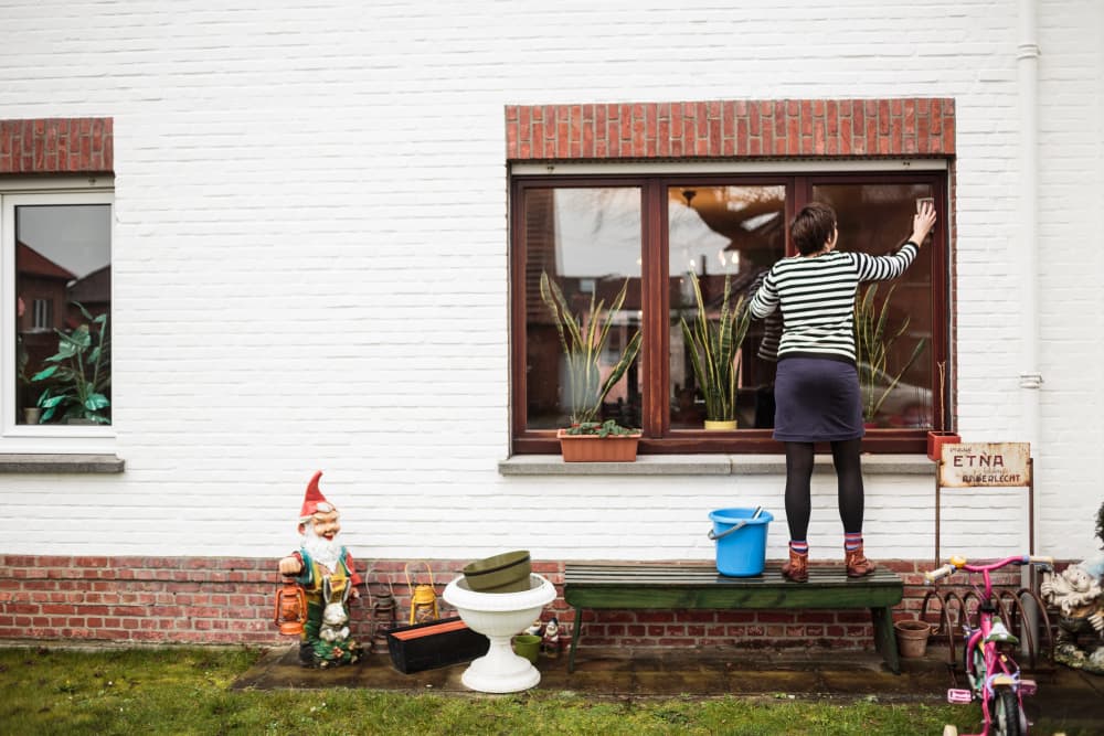 Vrouw poetst de ramen van een woning.