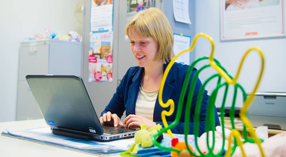Vrouw zit achter laptop aan bureau met kinderspeelgoed