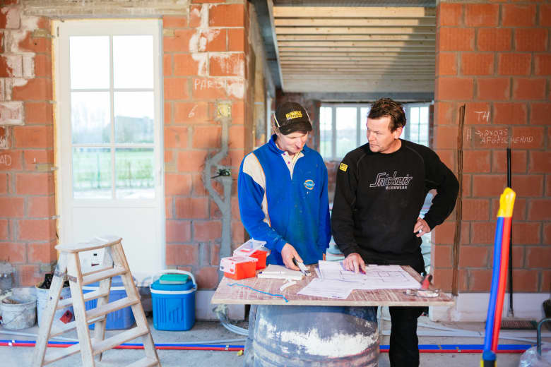Twee mannen  bespreken bouwplannen in het midden van een bouwwerf.
