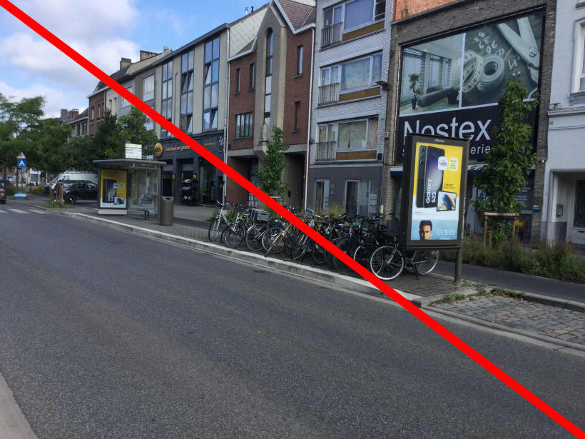 Een bushalte met op een groot deel van het perron fietsbeugels waaraan fietsen geparkeerd staan, vlak in de opstap- en afstapzone. Een rode streep op de foto geeft aan dat dat niet ok is.