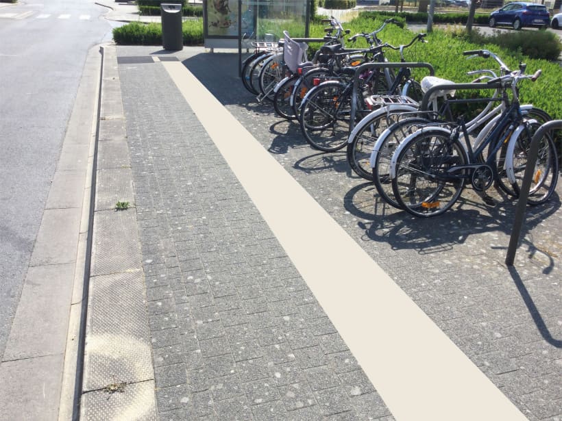Een lijn die bestaat uit tegels met ribbels loopt over het voetpad naast een fietsenstalling