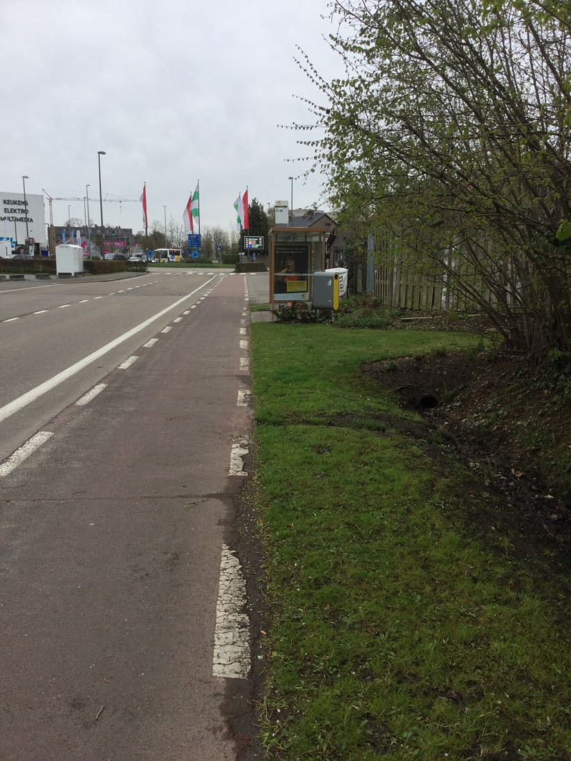 Een fietspad loopt tussen de rijweg en een bushalte. Een rode streep over de afbeelding doet begrijpen dat u deze situatie moet vermijden.