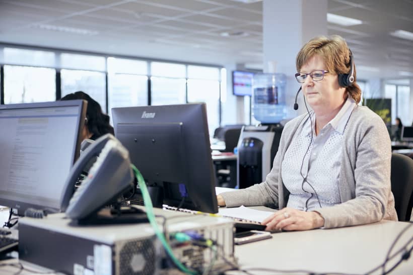 Vrouw met hoofdtelefoon aan een bureau in een contactcenter