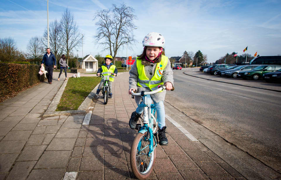 Een meisje fiets naar school. Ze draagt een fluovestje en fietshelm.
